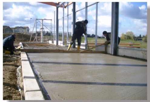 Bauarbeiter von Vierbau ziehen eine frisch gegossene Betonbodenplatte in einer Stahlbau-Halle ab.