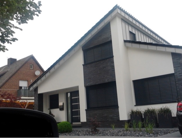 Modernes Einfamilienhaus mit weißem Putz, dunklen Klinkerbändern und Pultdach.