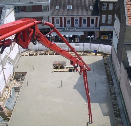 Rote Autobetonpumpe füllt die frisch geschalte Bodenplatte einer innerstädtischen Baustelle.